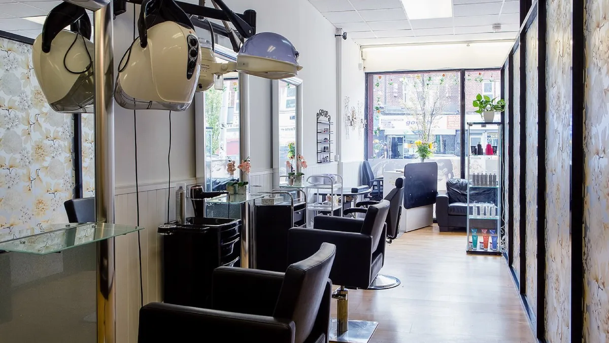 Inside the salon: a narrow room with black styling chairs, mirrors and a hooded dryer, daylight coming through the shopfront window