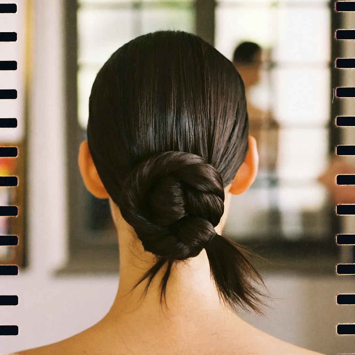 A finished updo, seen from behind, dark hair pinned in a smooth low twist
