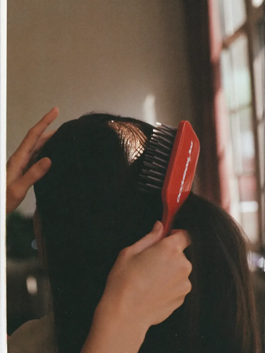 A hand brushing through freshly finished hair, daylight catching the shine